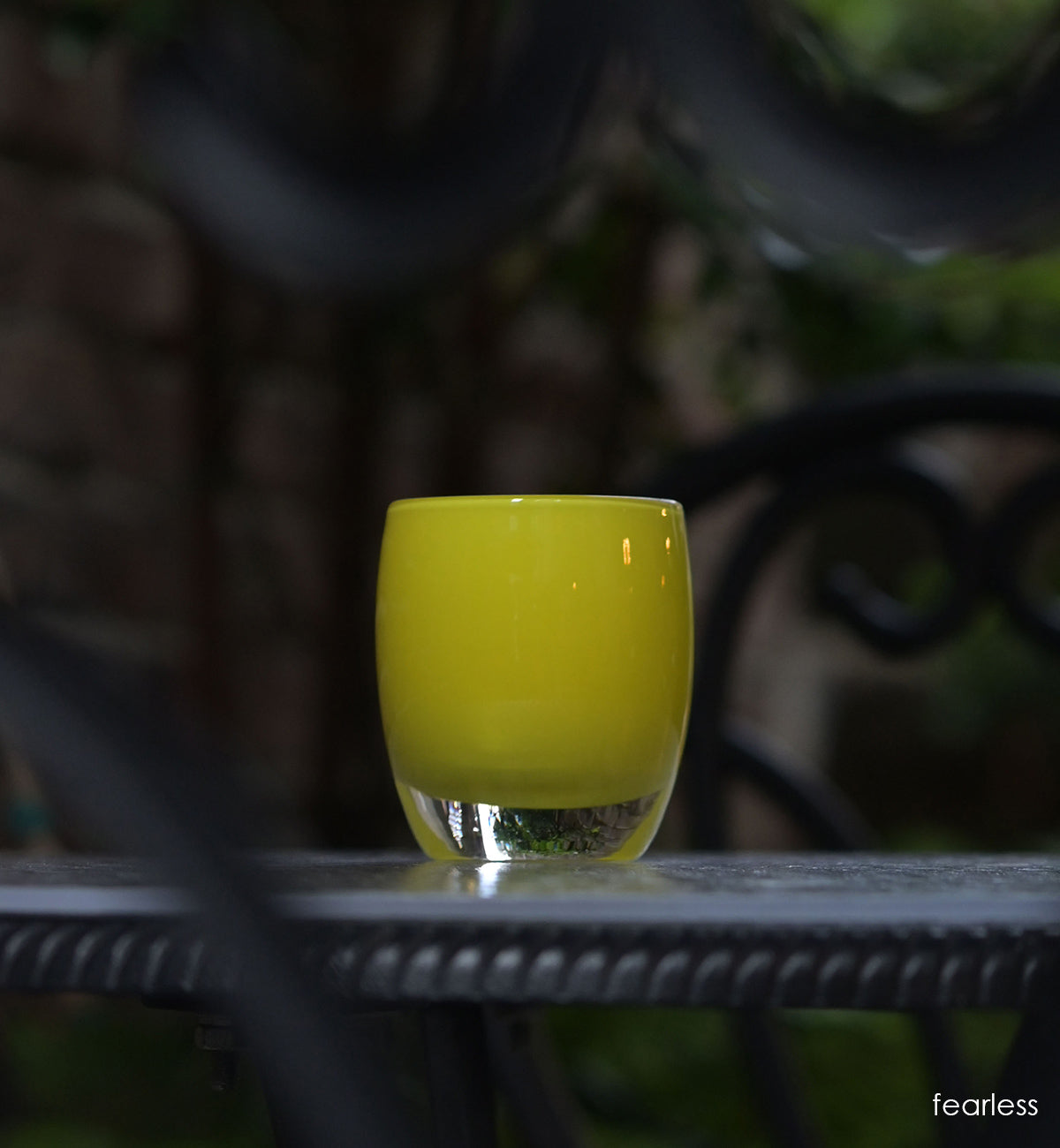 fearless bright yellow hand-blown glass votive candle holder on dark outside table.