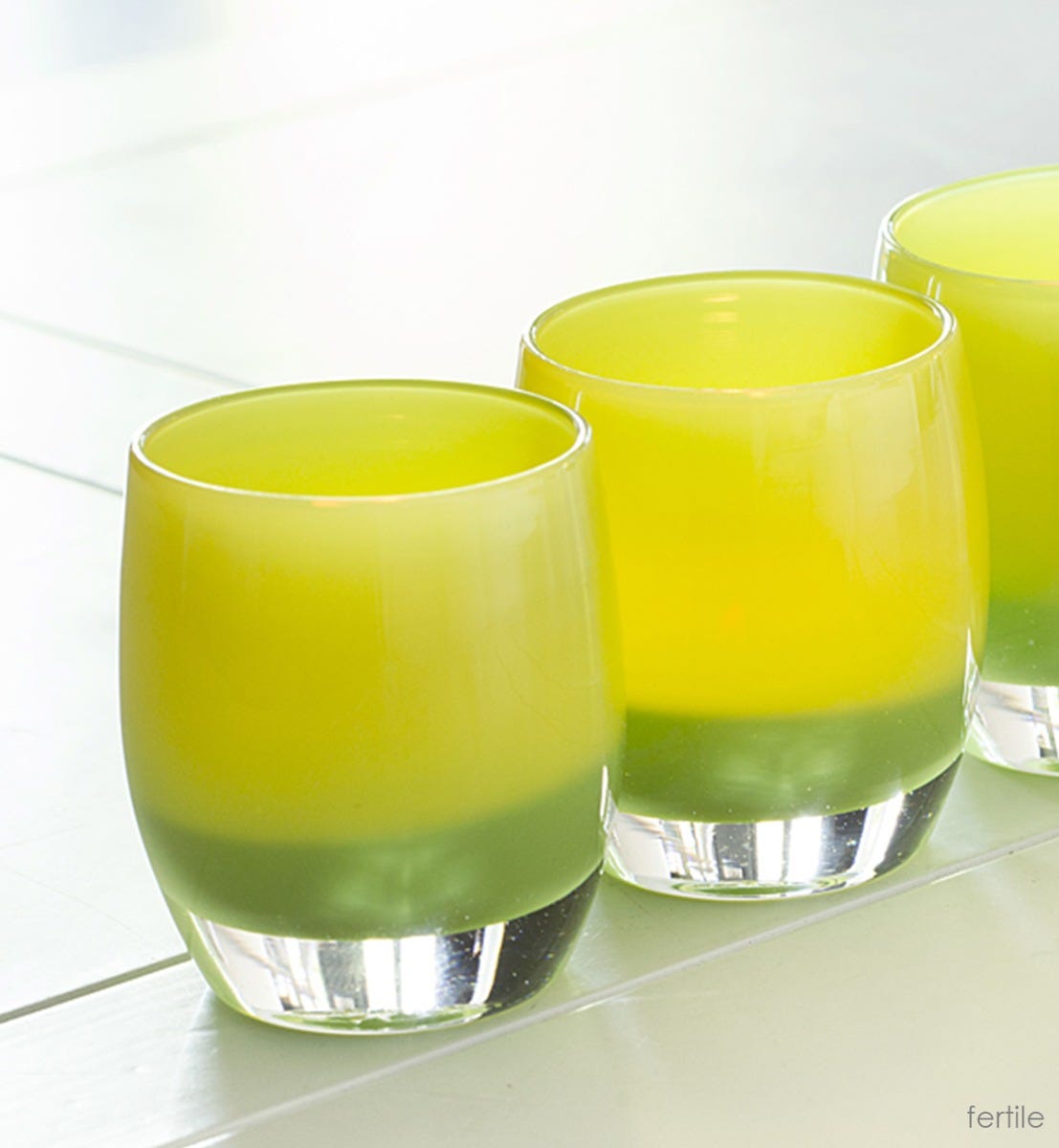 fertile patomic yellow green hand-blown glass votive candle holder on cream surface.