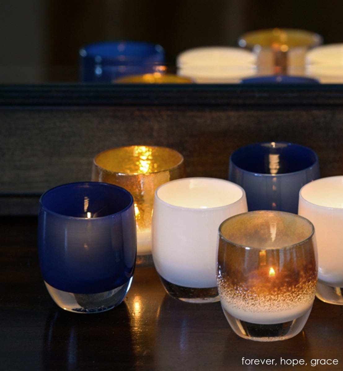 two forever deep navy blue hand-blown glass votive candle holders with hope and grace. on dark table in front of a mirror.