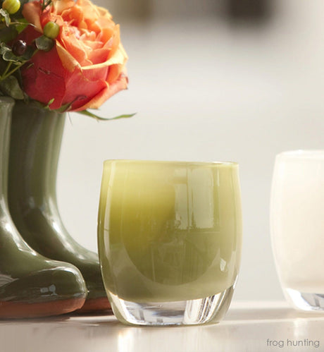 frog hunting moss green, hand-blown glass votive candle holder next to boot vase with flowers and white glassybaby.