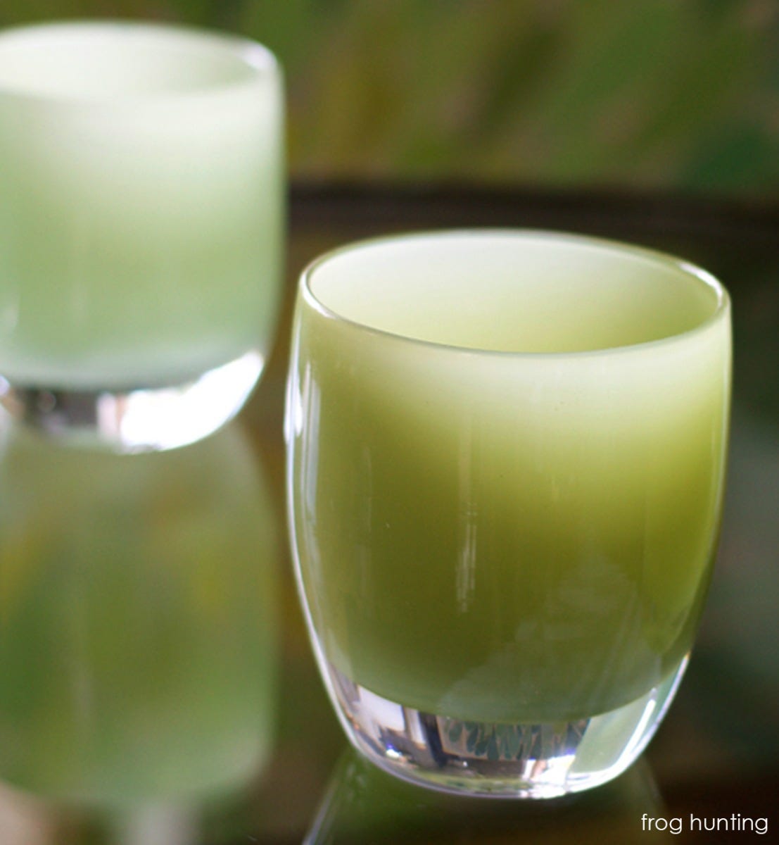 frog hunting moss green, hand-blown glass votive candle holder on reflective surface.