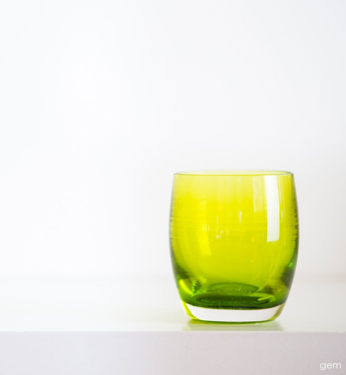 gem transparent green, hand-blown glass votive candle holder on white mantle with white background.