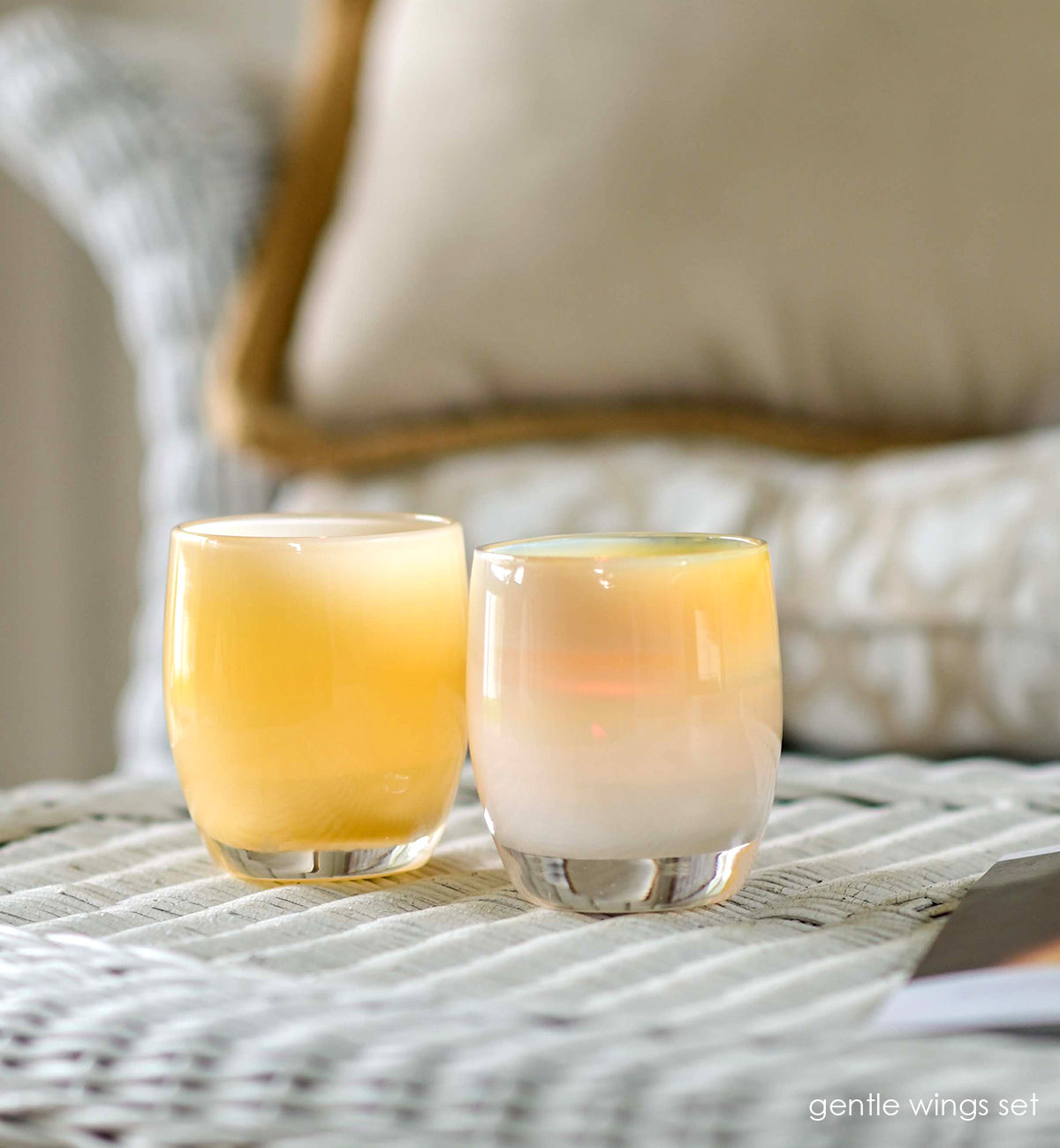 gentle wings set, angel and comfort hand-blown pale yellow set of two, hand-blown glass votive candle holders on a white wicker chair.