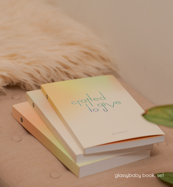 coffee table books of glassybaby volume collection on an ottoman with sheepskin and plant in corner.
