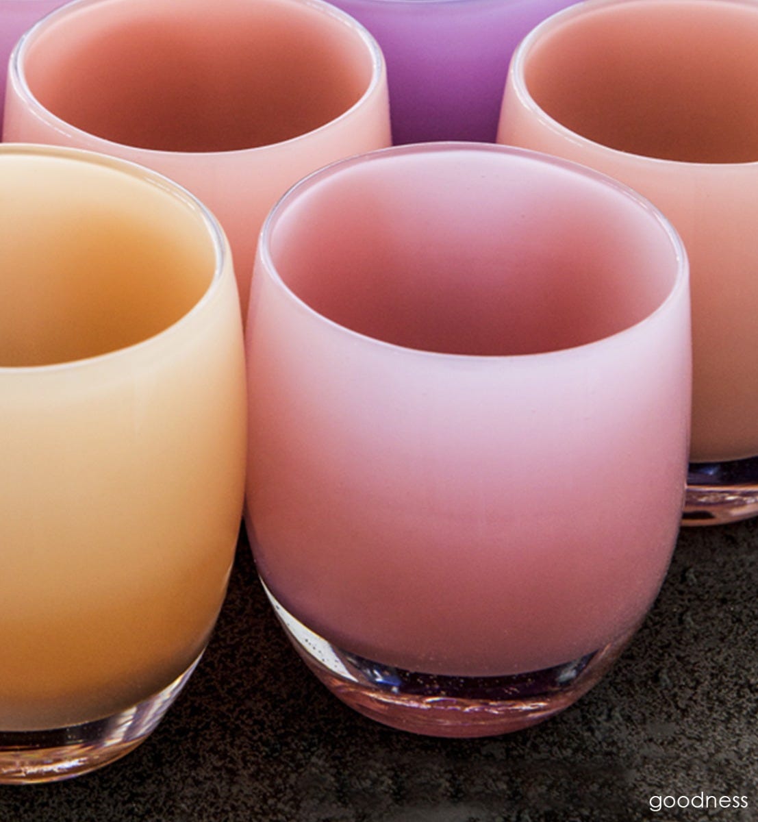 goodness opaque pink hand-blown glass votive candle holder with other votives on a dark surface.