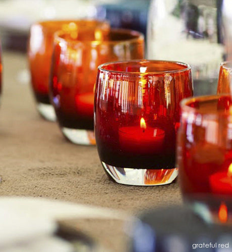 several grateful red wine red with metallic interior hand-blown glass votive candle holders on a dining room table canvas runner.