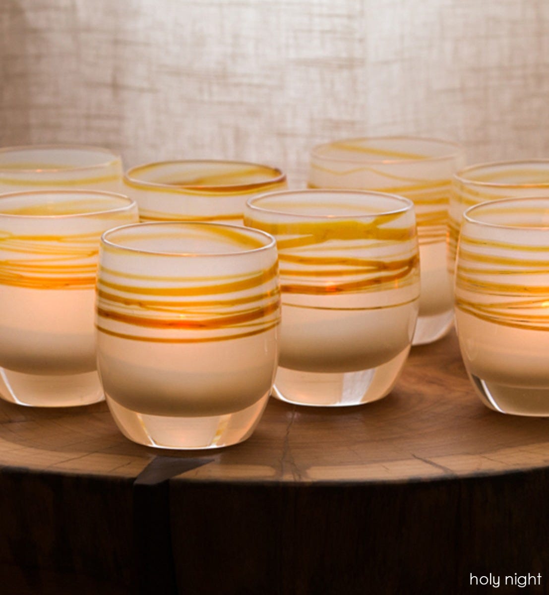 several holy night white brown with purple gold metallic wrap, hand-blown glass votive candle holders on a tree stump table.