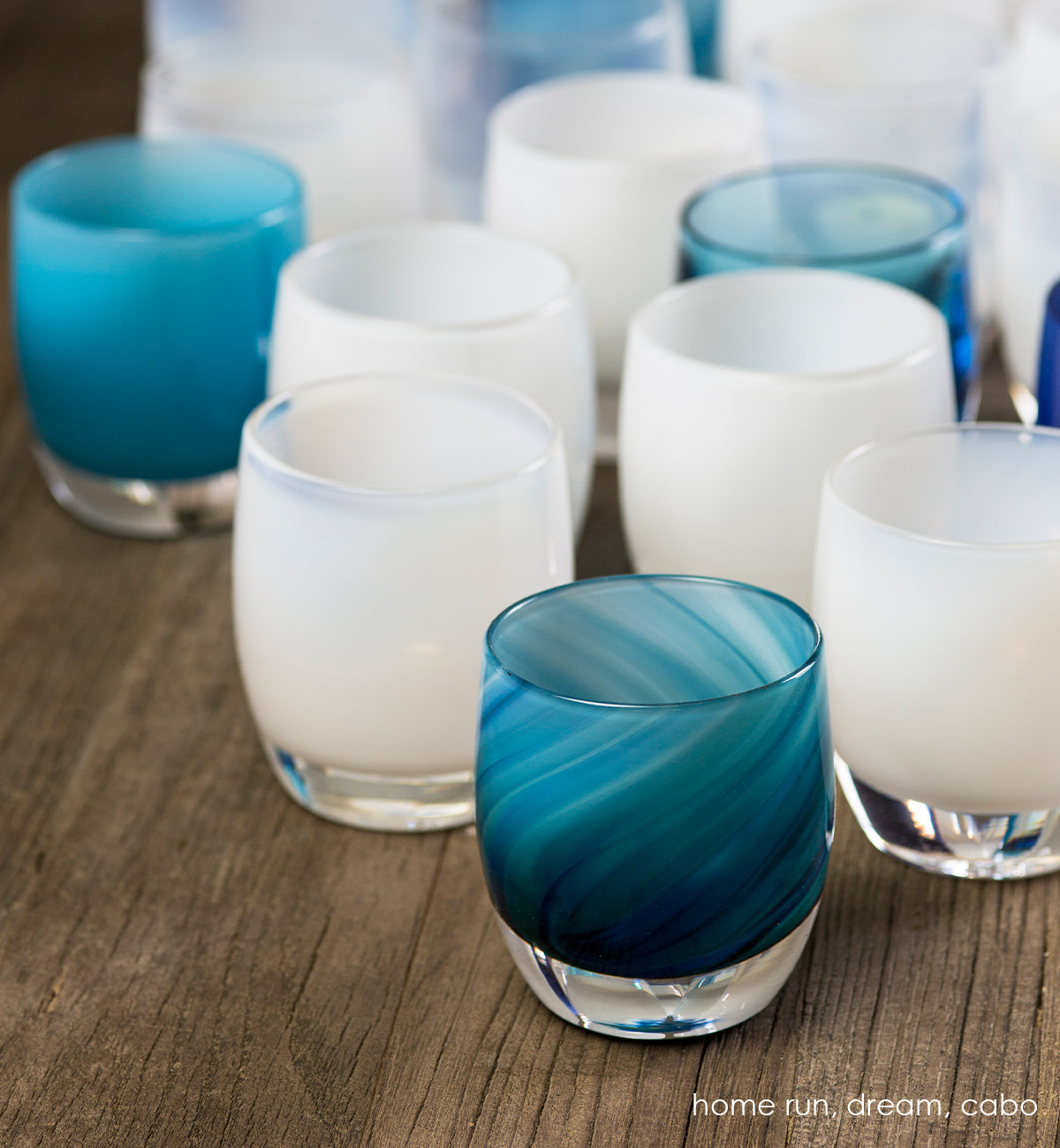 home run blue swirl, hand-blown glass votive candle holder in a grouping with dream and cabo on a wood surface.