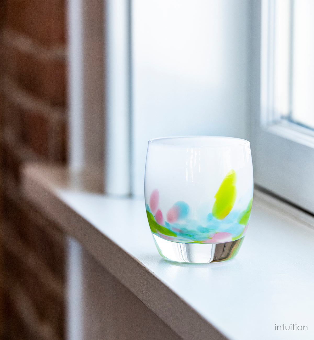 white hand-blown glass candle holder with blue, green and pink petals of color at the base.