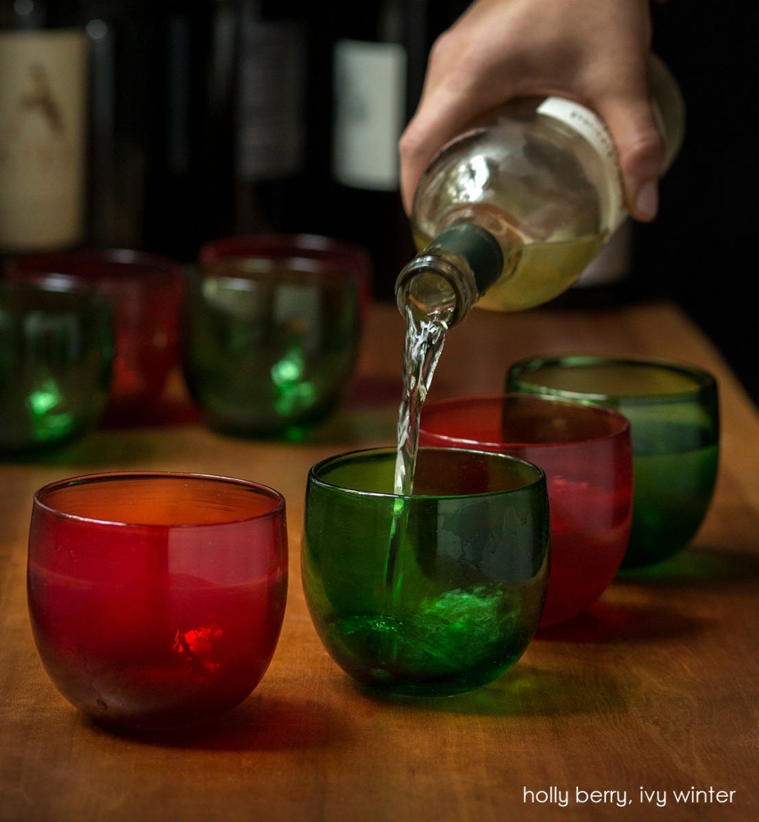 several ivy winter drinkers transparent green hand-blown drinking glasses with holly berry drinkers, with wine being poured inside.