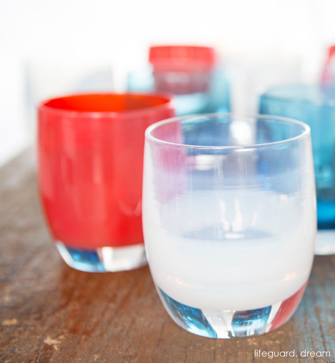 lifeguard hand-blown cherry red glass votive candle holder next to dream on a wood table.