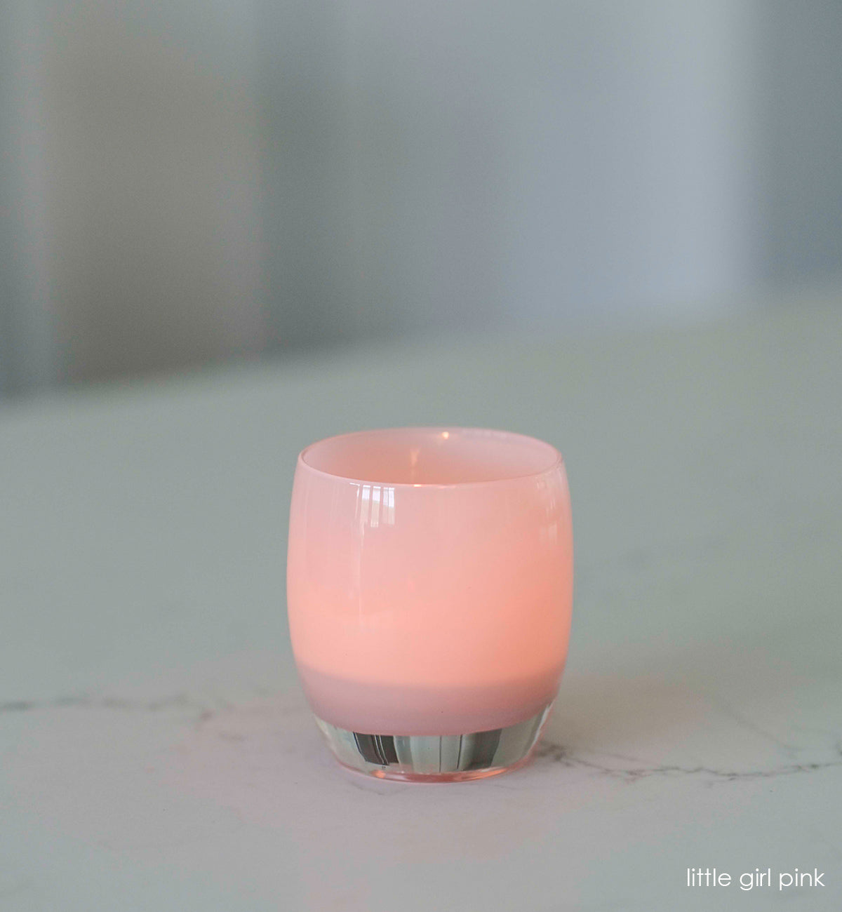 little girl pink, soft pink hand-blown glass votive candle holder on a marble countertop.