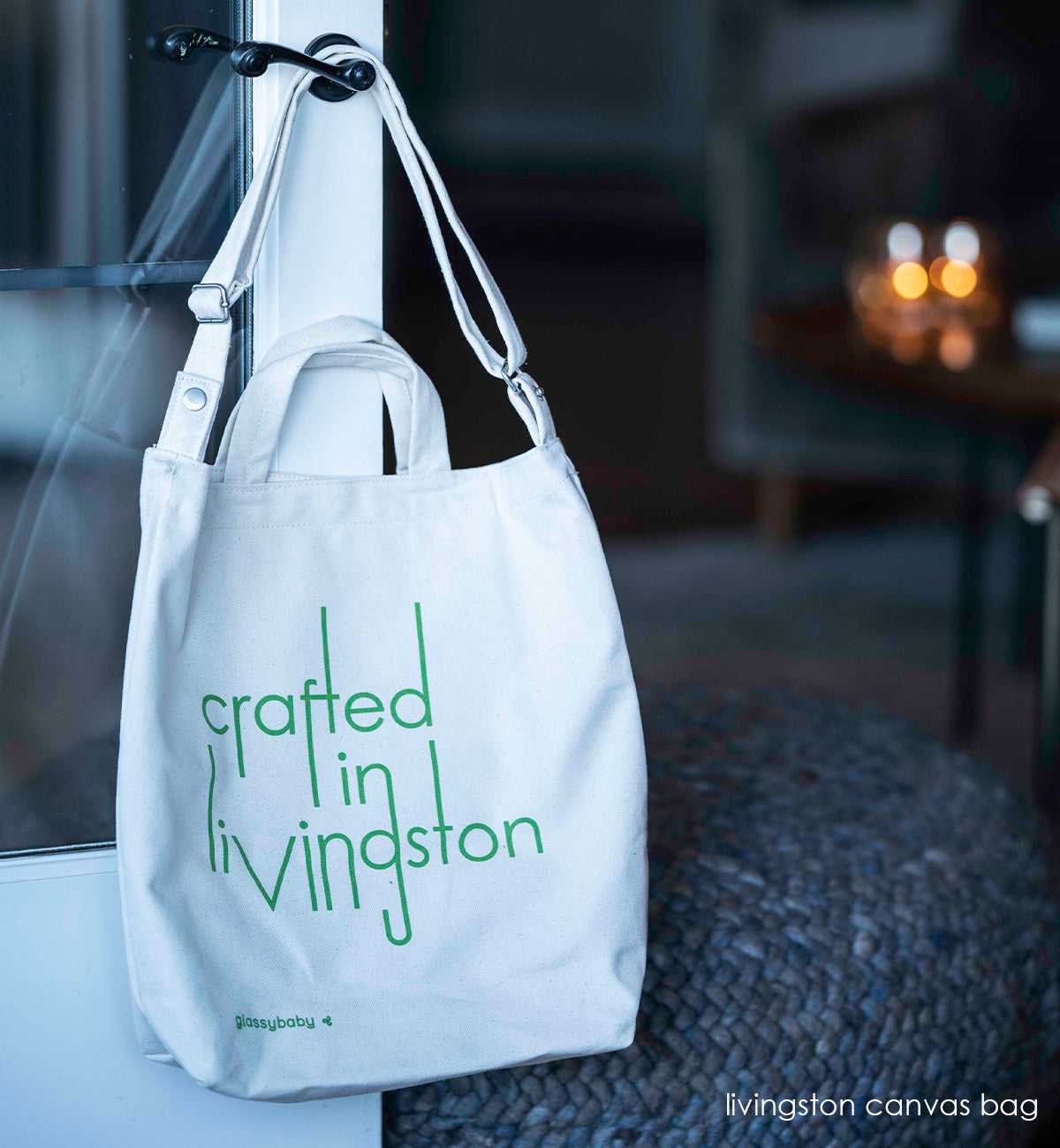crafted in Livingston canvas tote bag, hanging on a door handle with gray ottoman behind.