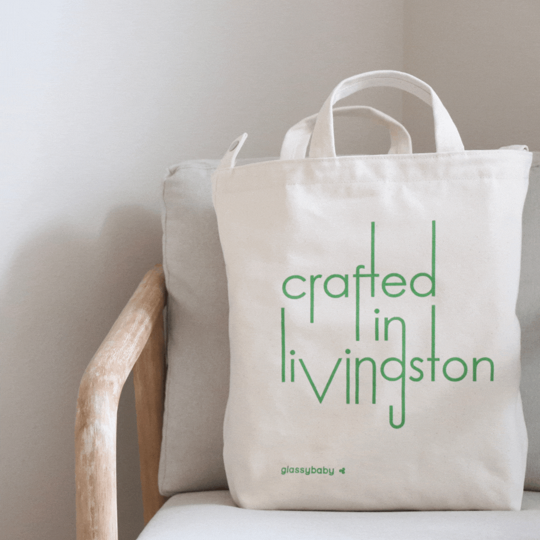 green "crafted in Livingston" canvas tote on a white and light wood chair.