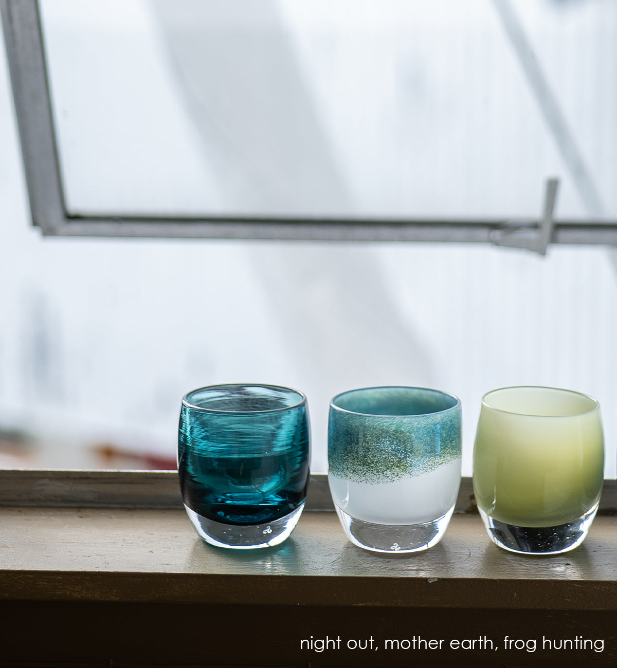 night out dark aqua blue transparent, hand-blown glass votive candle holder. paired with mother earth metallic blue green on white, and frog hunting green on an open windowsill.