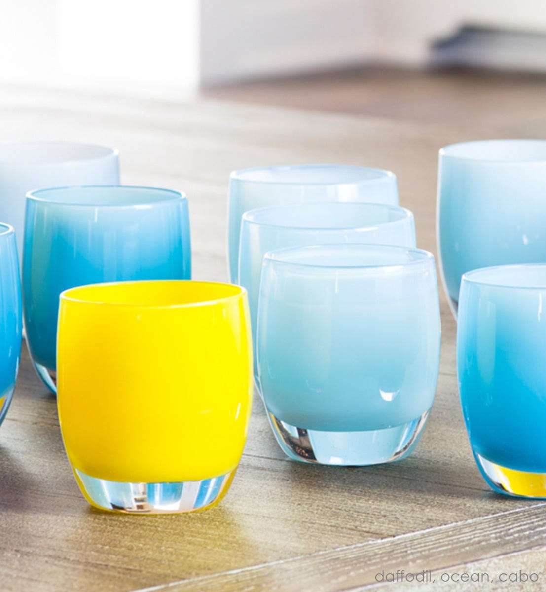 ocean light blue hand-blown glass votive candle holders with daffodil and cabo on a light wood surface.