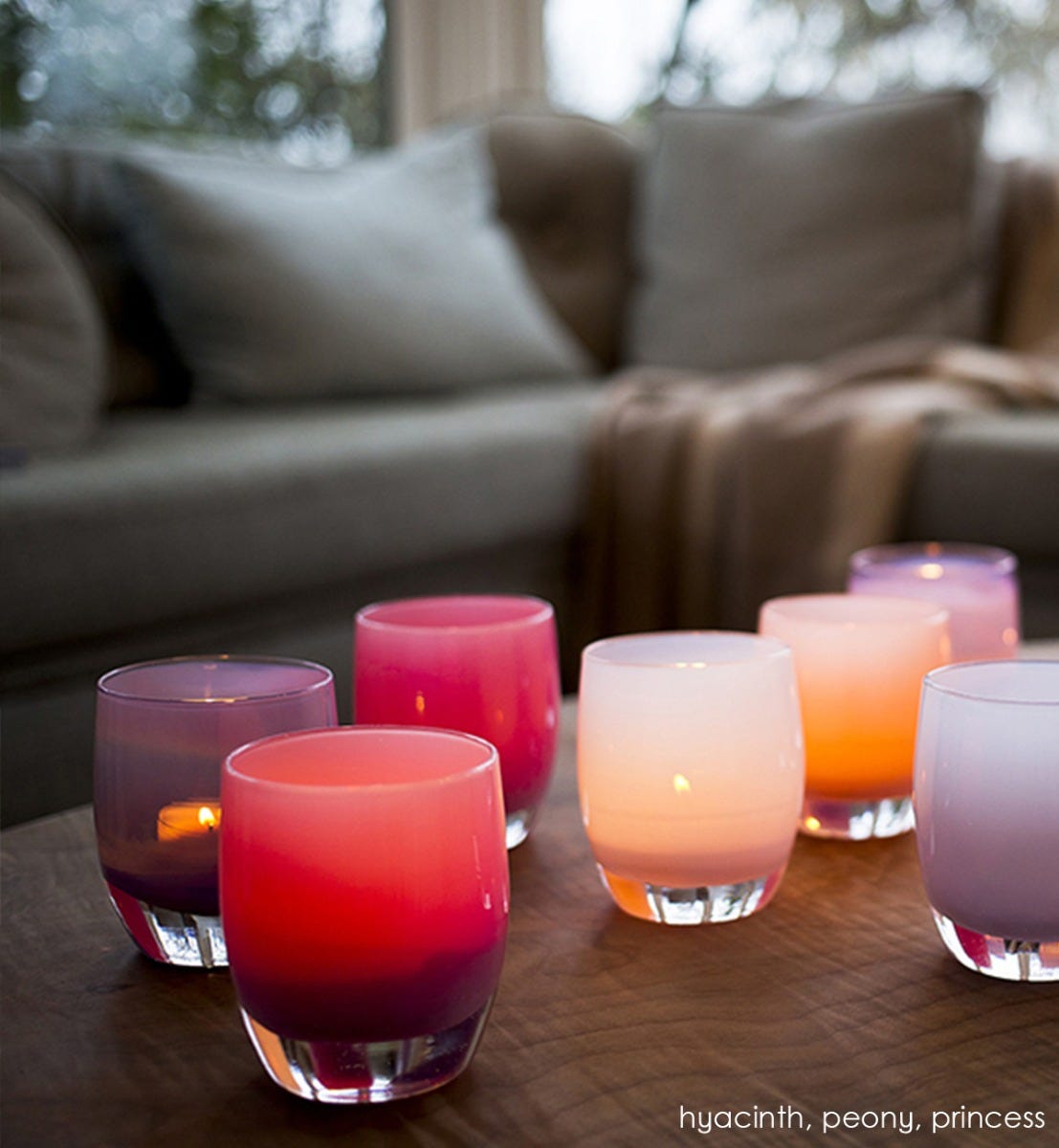 peony pink hand-blown glass votive candle holder with hyacinth and peony on a gray ottoman with a gray couch in background.