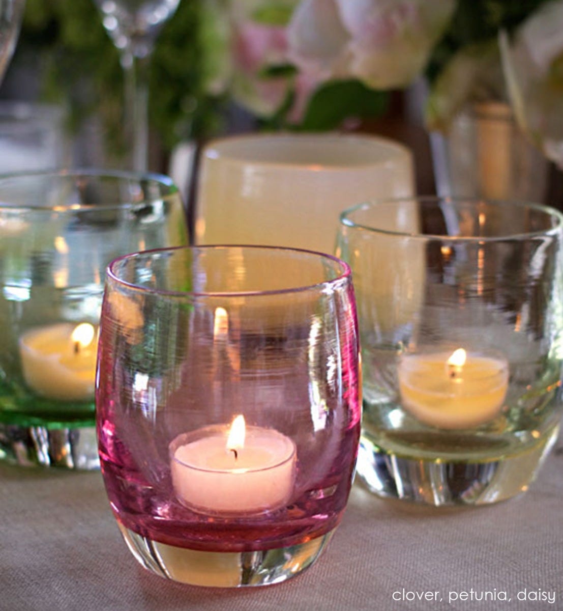 petunia transparent light pink hand-blown glass votive candle holder next to clover and daisy on a dining room table runner.