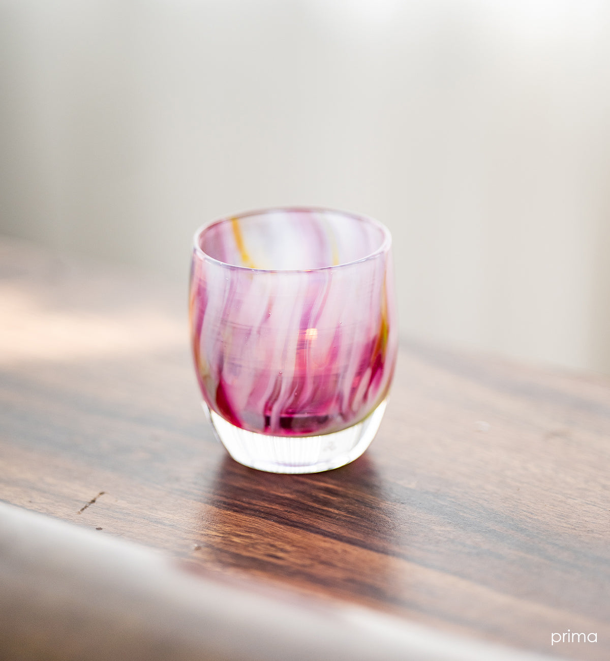 prima pink multi-colored petal, hand-blown glass votive candle holder on a wood surface.