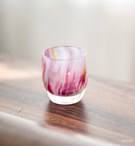 prima pink multi-colored petal, hand-blown glass votive candle holder on a wood surface.