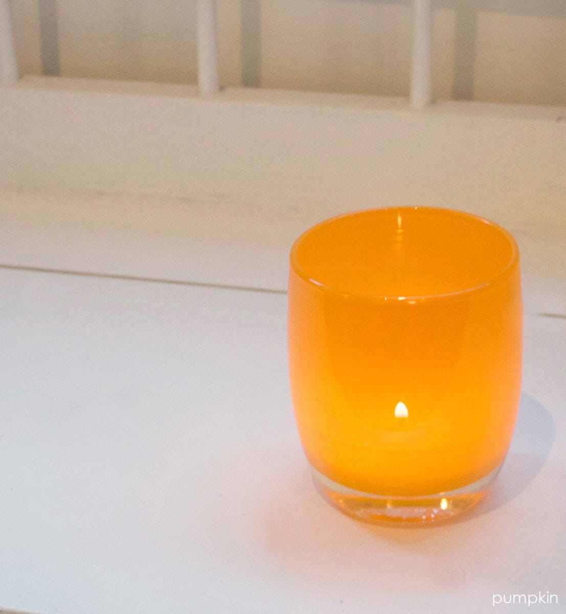 pumpkin orange hand-blown glass votive candle holder with a lit tealight on a white surface.