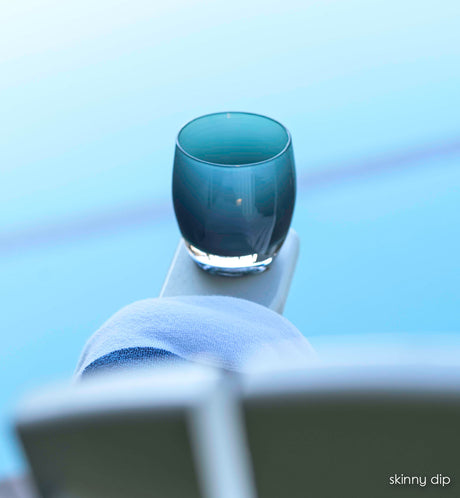 skinny dip, dark teal hand-blown glass votive candle holder perched on a pool chair next to a beach towel.