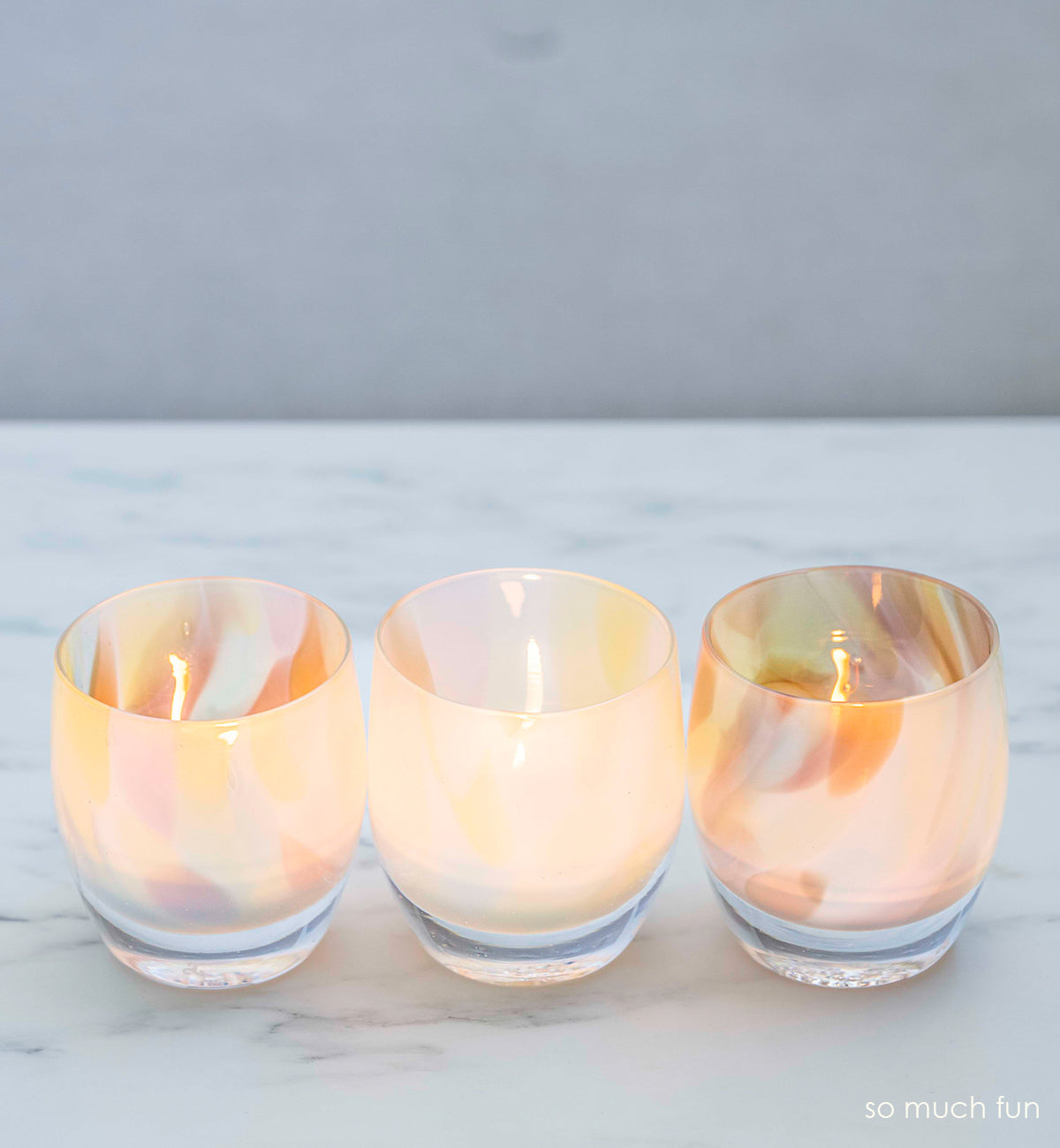 three so much fun, pastel mix, hand-blown glass votive candle holders on a marble surface.