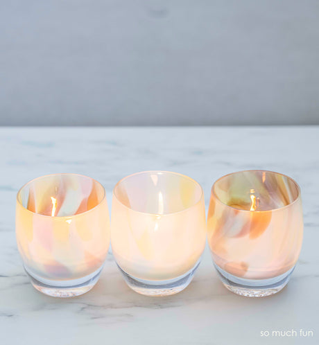 three so much fun, pastel mix, hand-blown glass votive candle holders on a marble surface.