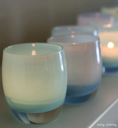 sorry, light blue, hand-blown glass votive candle holder with stormy on cream surface.