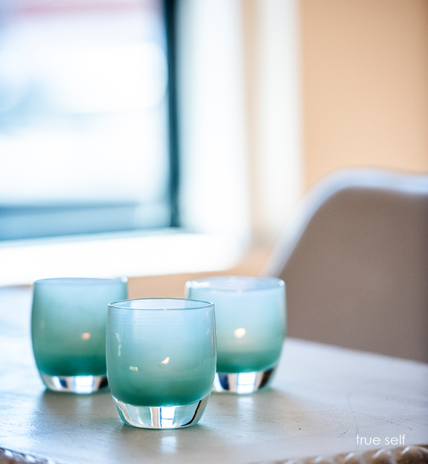 two true self, opaque translucent seafoam green, hand-blown glass votive candle holders on a cream living room table.