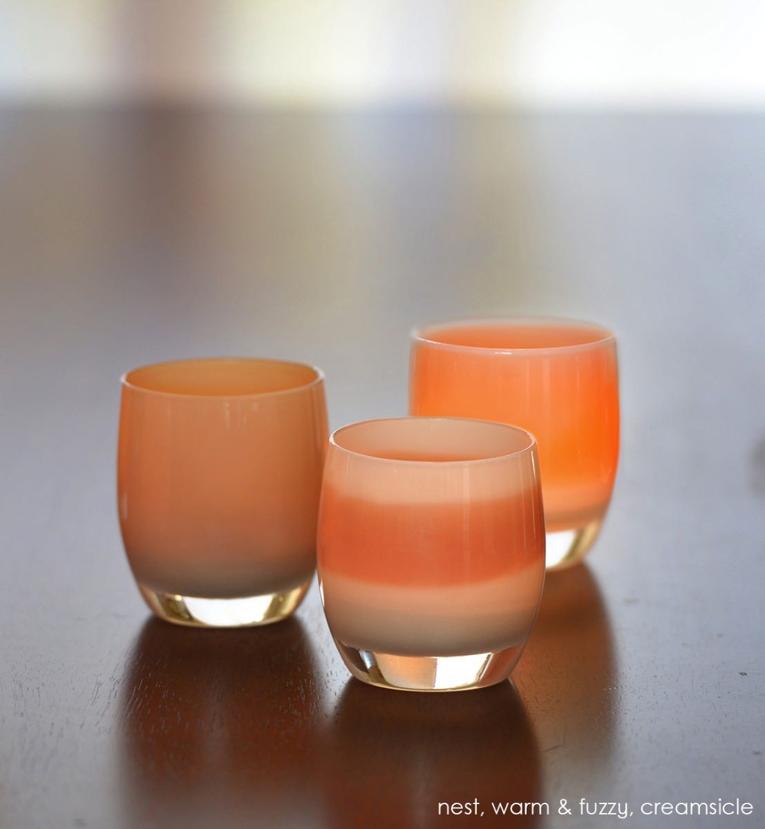 warm and fuzzy, cream glass with burnt orange stripe, hand-blown glass votive candle holder. Paired with nest and creamsicle on a dark wood table.